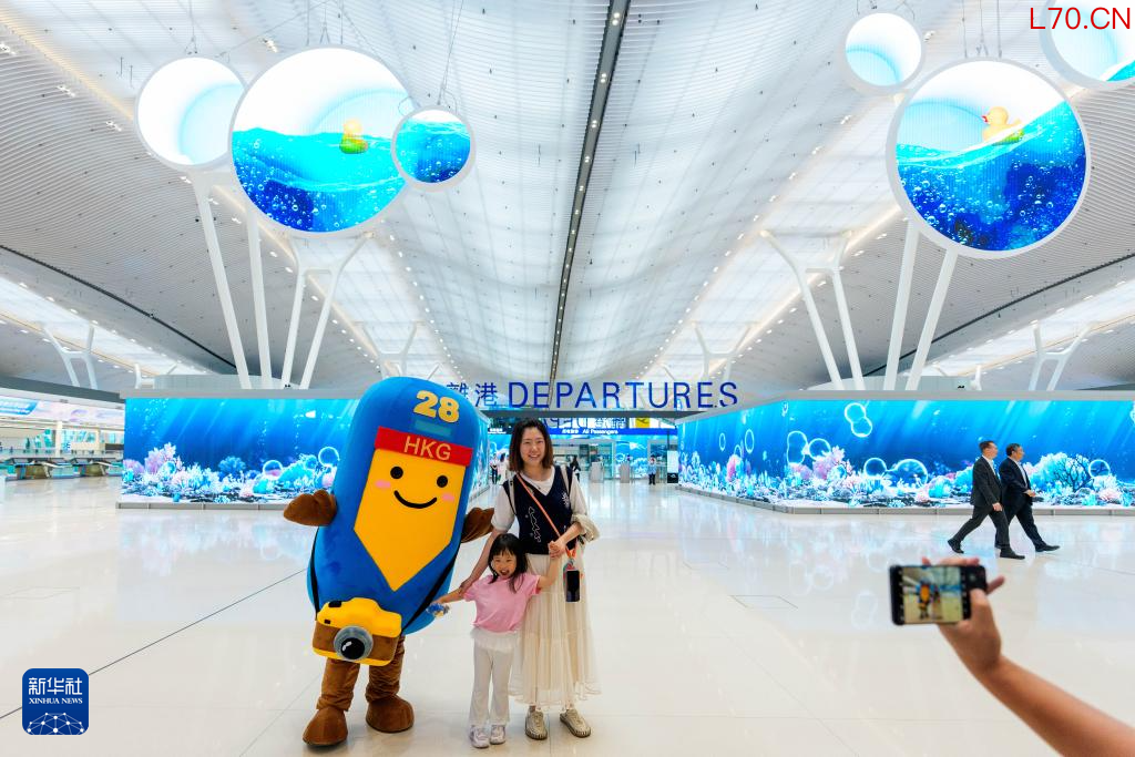 5月27日,旅客在香港国际机场二号客运大楼离境大堂与机场吉祥物合影。新华社记者 朱炜 摄
