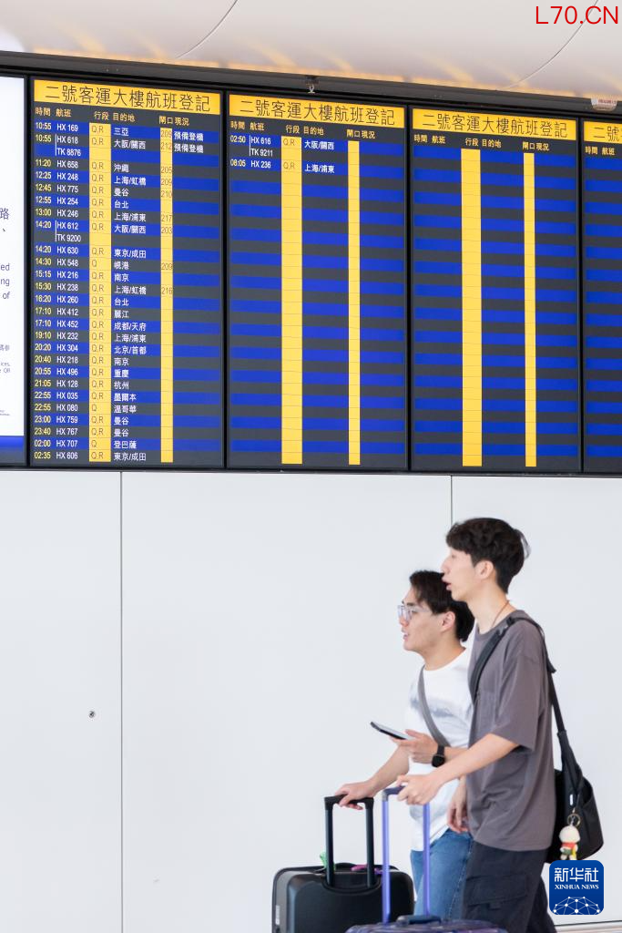 5月27日,旅客从香港国际机场二号客运大楼离境大堂航班信息显示屏前走过。新华社记者 朱炜 摄